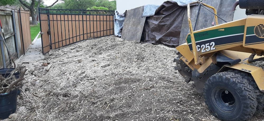 Excavator working on a cleared area with debris and tarps near a gated fence.