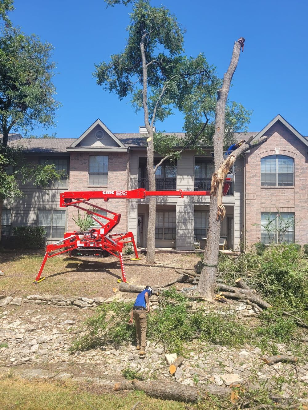 Tree removal in progress with a red crane at an apartment complex, workers clearing debris.