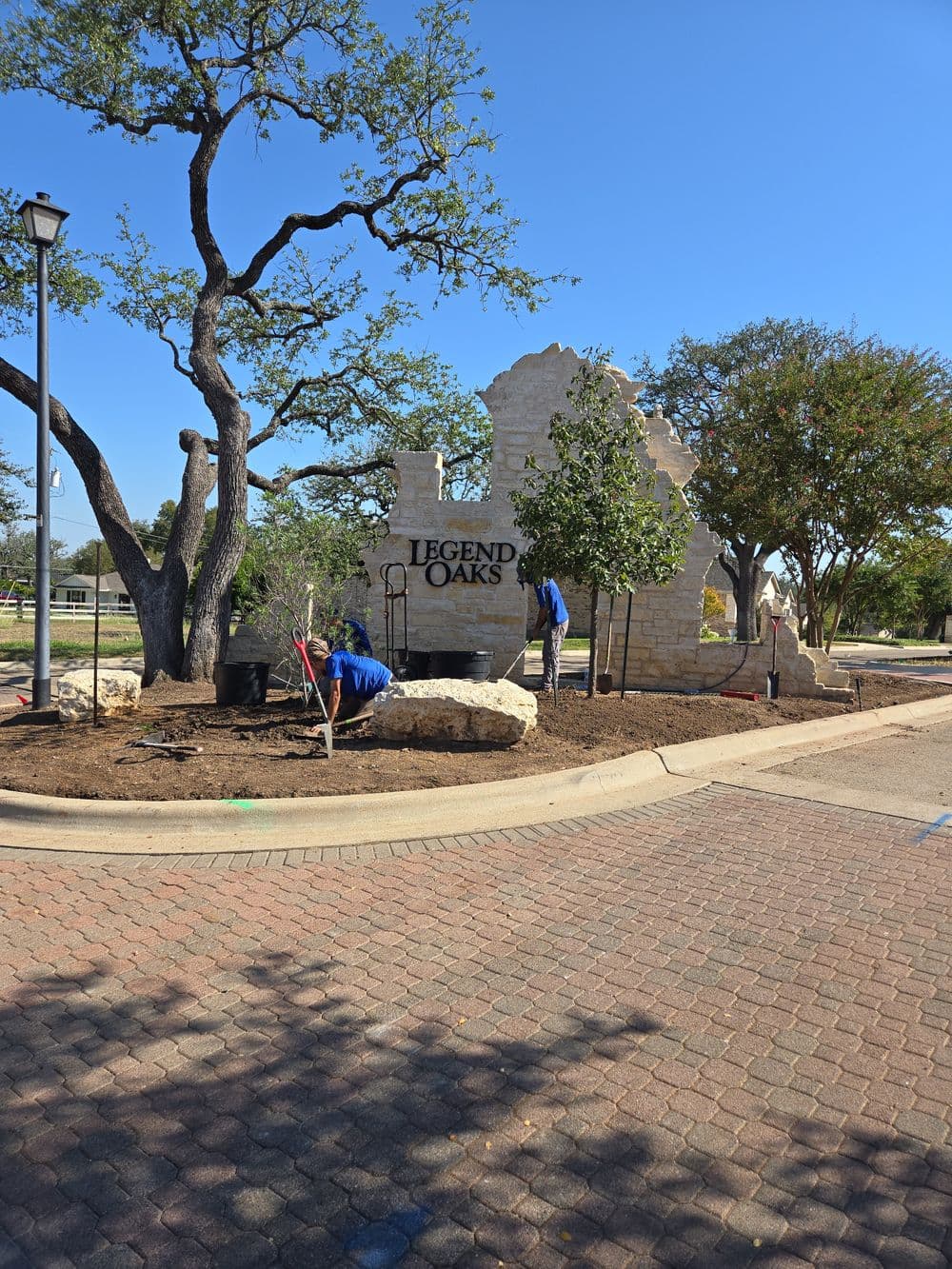 Workers landscaping around the Legend Oaks entrance sign on a sunny day.