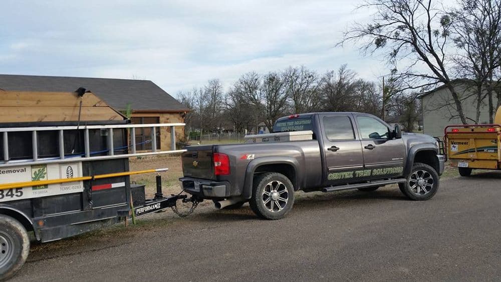 Silver pickup truck with trailer parked by a construction site in a rural area.