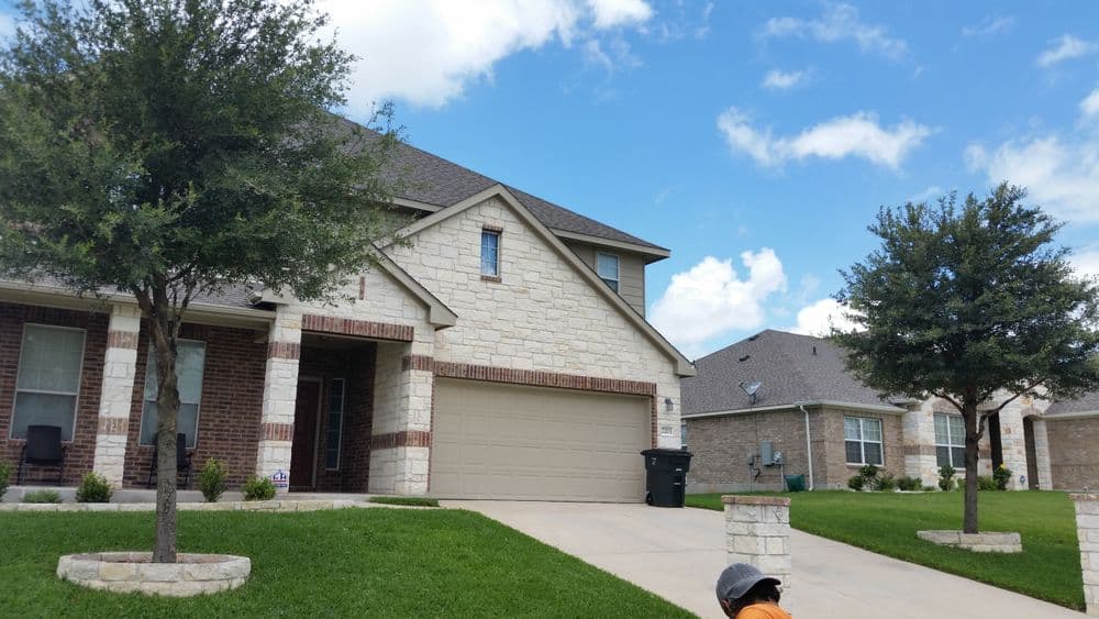 Two-story home with stone facade, green lawn, and clear blue sky overhead.