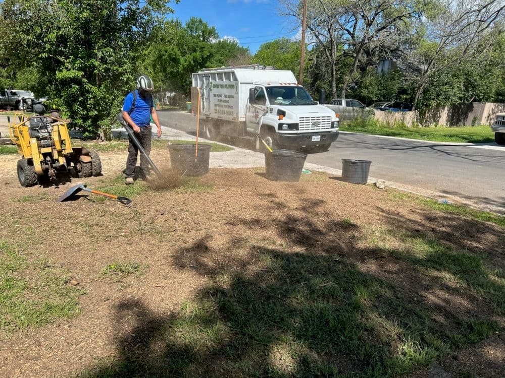 Person landscaping a yard with equipment and buckets near a work truck on a sunny day.