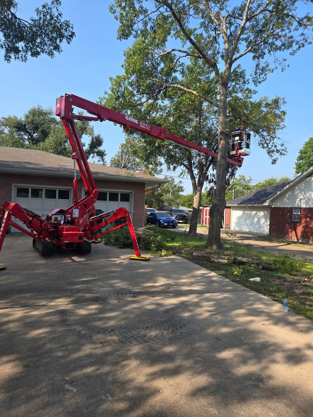Red cherry picker lifting a worker to trim a tree near a residential home.